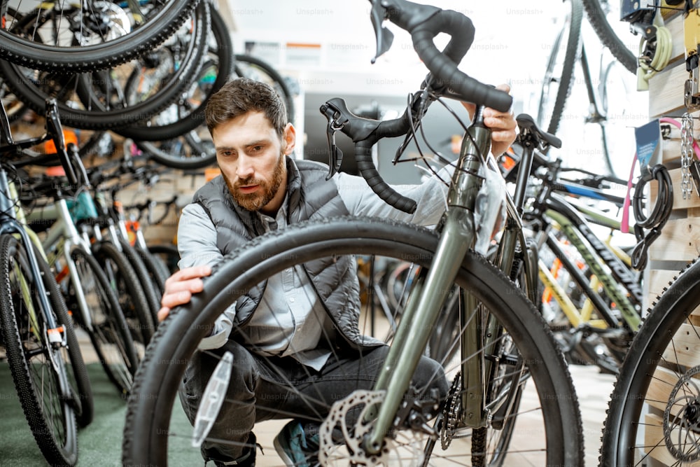 Mann wählt neues Fahrrad aus, um im Laden stehend mit vielen Fahrrädern und Sportgeräten drinnen zu kaufen