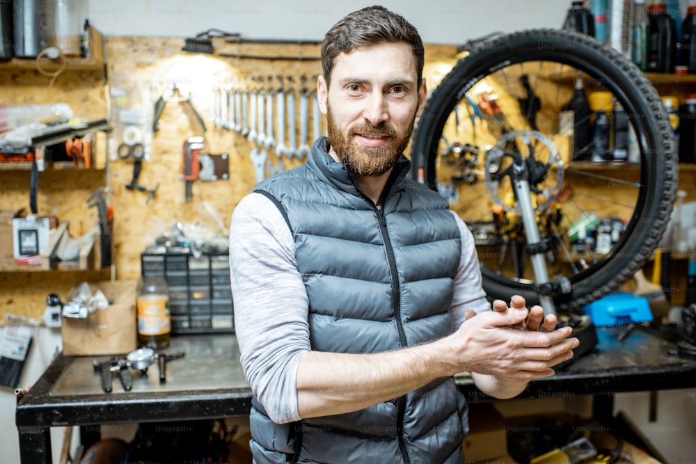 Portrait of a handsome repairman standing in the bicycle workshop with working tools on the background