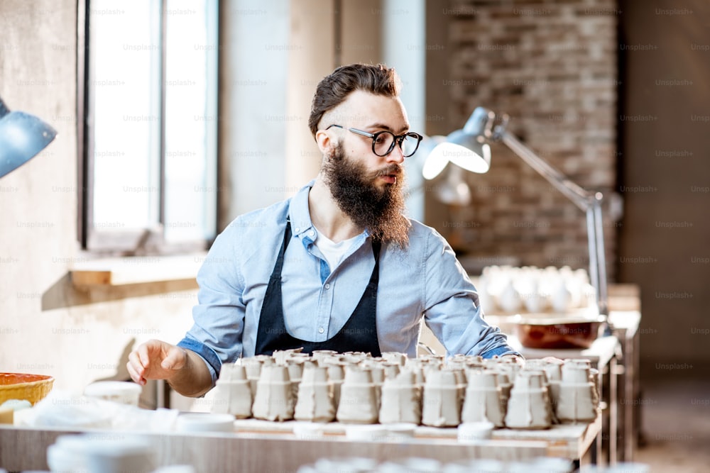 Hombre barbudo guapo trabajando con piezas de cerámica en el lugar de trabajo en la tienda de cerámica