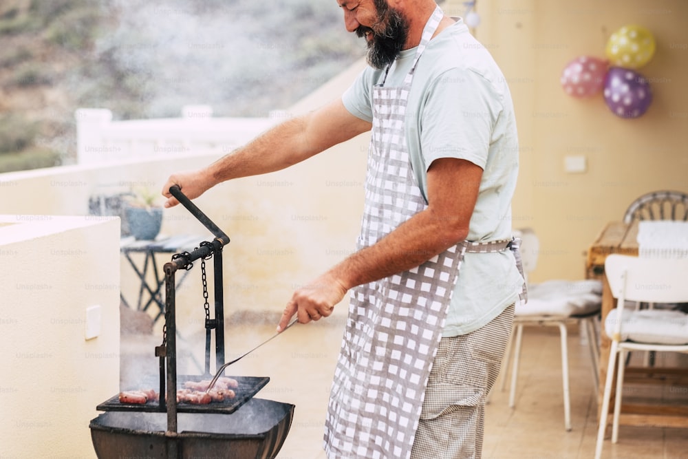 Close up of man hands cooking fresh meat on a old style wood and fire barbecue bbq grill - home celebration for people love to eat and enjoy with friends - restaurant and home cook and food