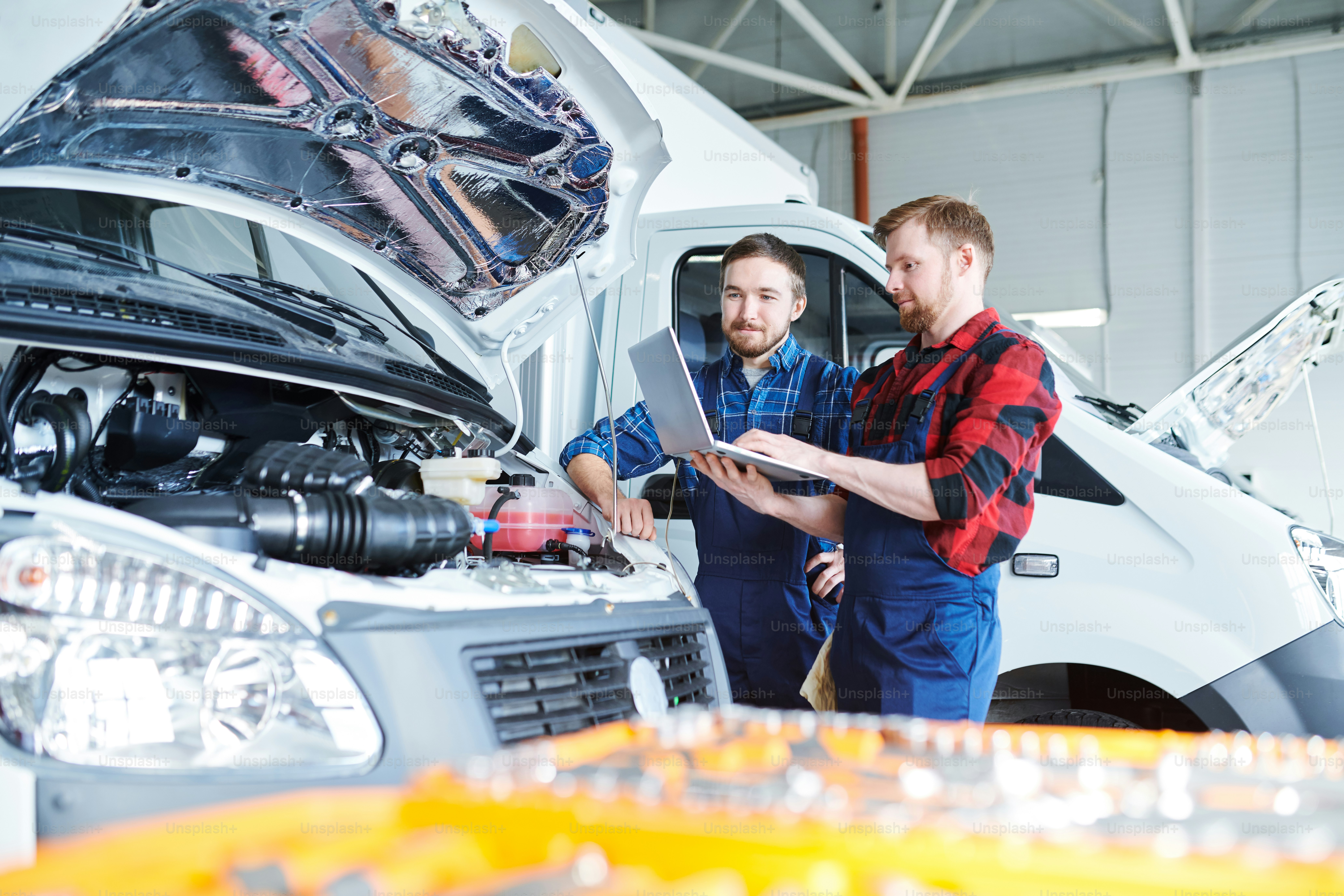 Dois jovens reparadores em roupas de trabalho de pé ao lado do motor do carro e sites de consultoria para informações de manutenção