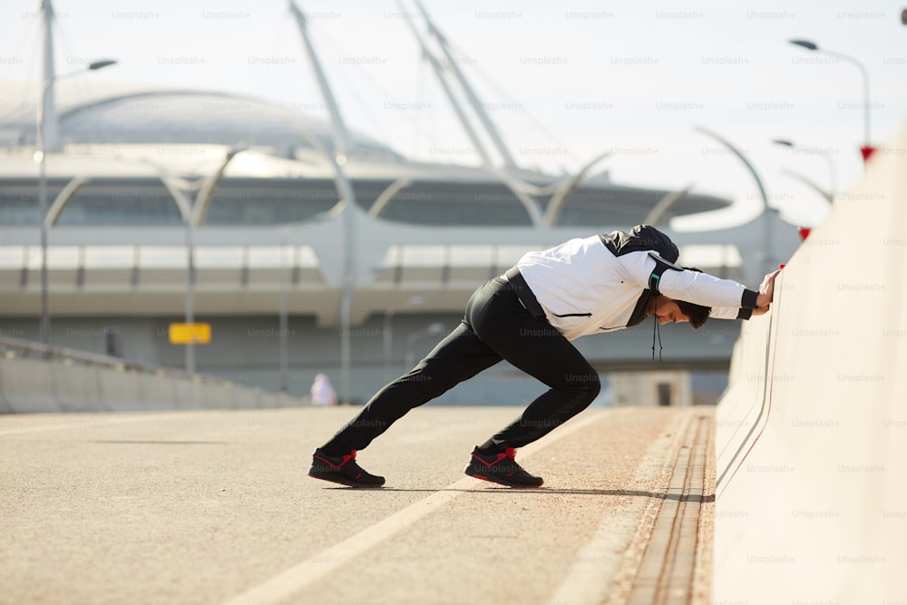 スタジアムで足と腕の運動をしながら橋の境界にもたれかかる若い強いスポーツマン