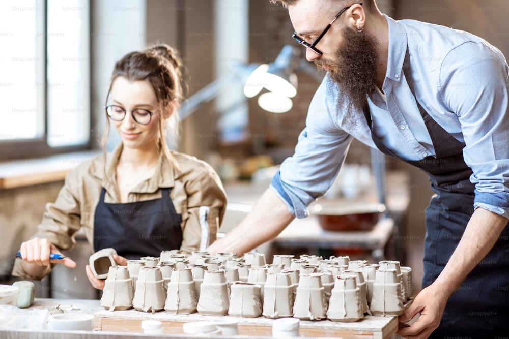 Man and woman working with clay workpieces making ceramic products at the working place of the pottery shop