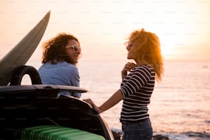 美しい人々の友人夫婦の巻き毛の女性が一緒に旅行を楽しみ、海の夕日を楽しむ – 幸せな女性と車と荷物を持つ夏休みの休暇のコンセプト