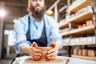 Homem bonito como um trabalhador de oleiro em avental fazendo jarros de barro na roda de cerâmica na pequena fabricação