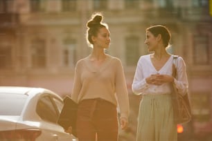 Two young friendly casual women moving down street after visiting cafe and discussing news or working points