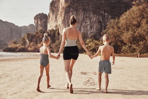 Rearview of a Mother and her two children walking hand in hand together along a sandy beach during summer vacation