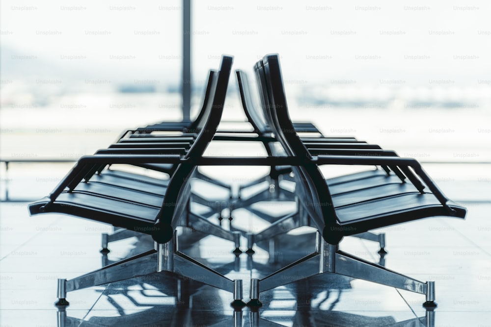 View of two rows of plastic seats indoors of a modern airport terminal or a railway station depot with a huge window behind, shallow depth of field, selective focus on the closest armchairs