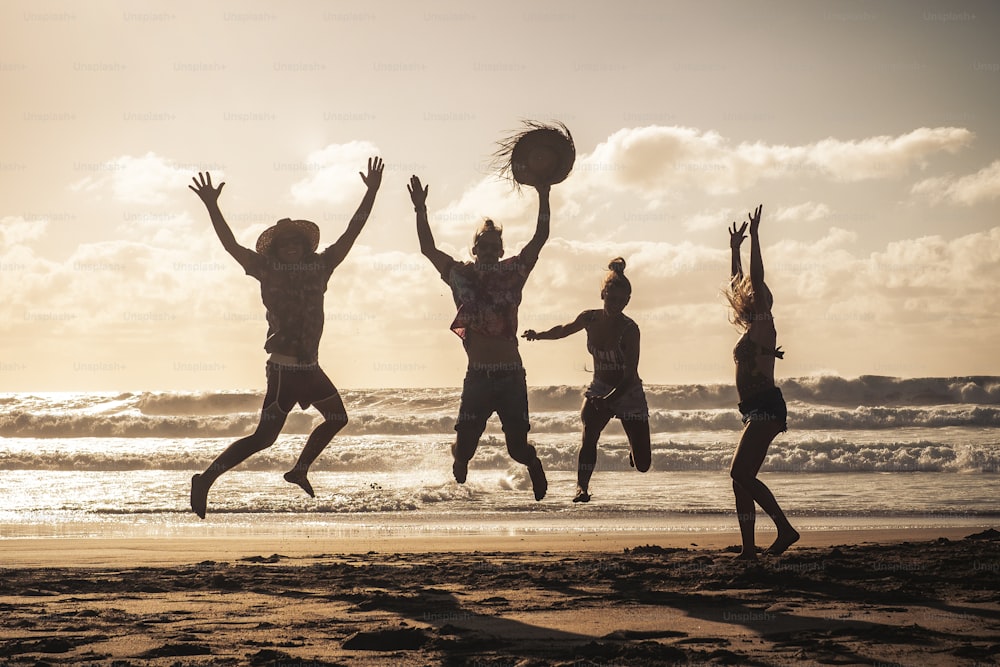 Sunset at the beach with happy group of young people jumping having fun - friends on summer holiday vacation enjoying together in friendship - sandy lifestyle and tourist travel concept