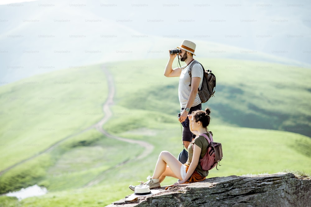 Couple enjoying beautiful landscape views, resting on the rock while traveling in the mountains during the summer time
