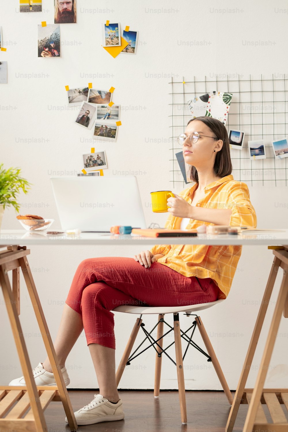 캐주얼 웨어를 입은 젊은 현대 사업가는 책상 옆에 앉아 차나 커피를 마시며 노트북 앞에서 영감을 얻습니다.