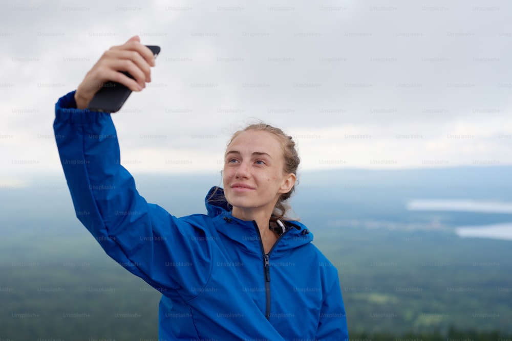 Portrait of pretty sports woman taking selfie on the top of the mountains after climbing with scenic view