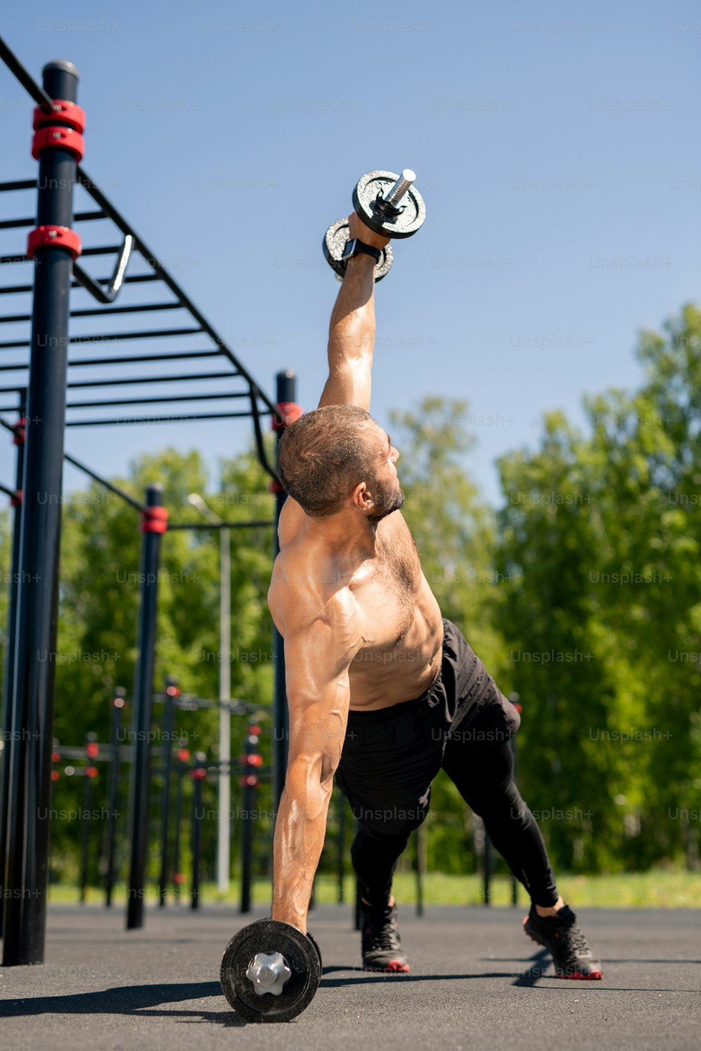 젊은 근육질의 보디빌더는 운동 중 무거운 바벨을 들면서 운동장에서 야외에서 훈련합니다.