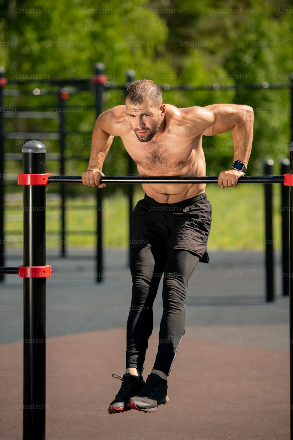 Young muscular athlete bending over sports bar while hanging over ground during physical exercise