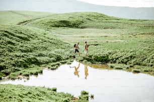 Hombre y mujer caminando cerca del lago en las montañas, vista del paisaje en el prado verde con lago durante el día soleado