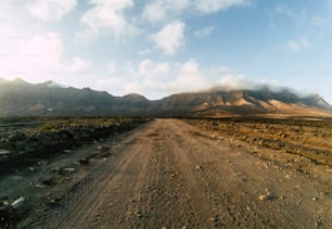 Long off road terrain way road viewed from ground level with mountains and blue cloudy sky - travel and adventure concept for alternative vacation and lifestyle