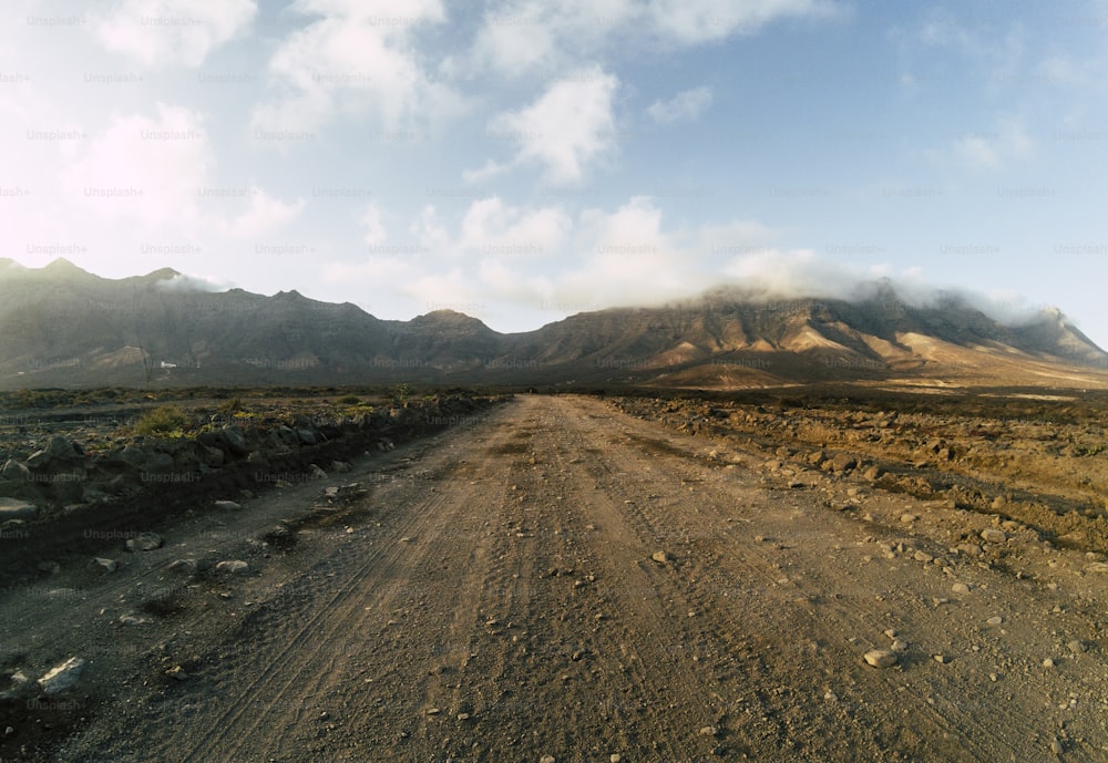 Long off road terrain way road viewed from ground level with mountains and blue cloudy sky - travel and adventure concept for alternative vacation and lifestyle