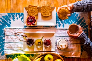 Breakfasy healthy morning time viewed from vertical above view  people woman with toasted bread and marmalades on a wooden tble drinking cappuccino coffee - focus on marmalades
