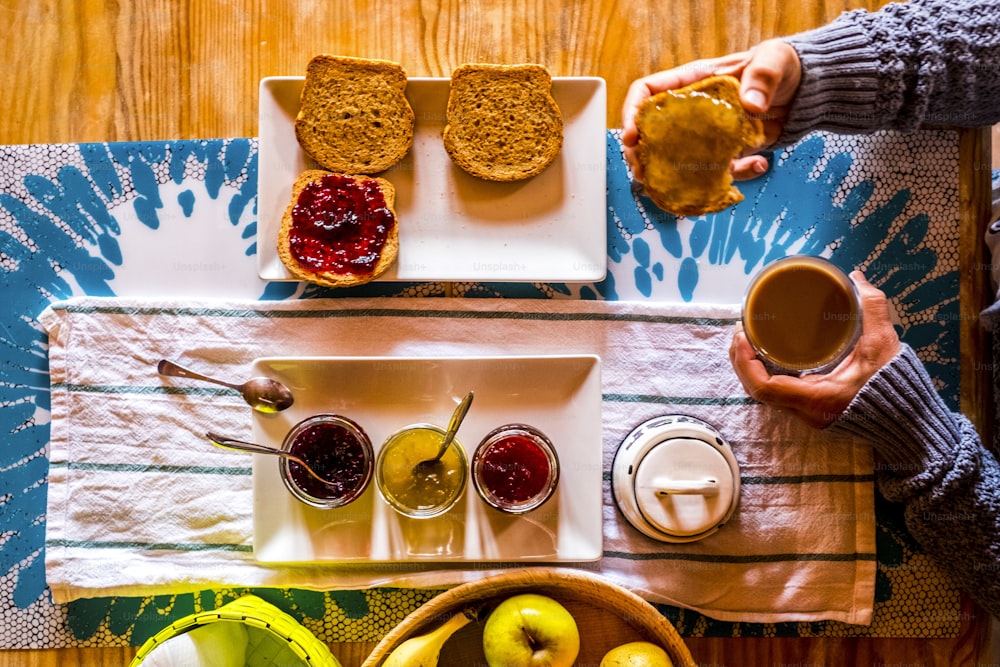 Breakfasy healthy morning time viewed from vertical above view  people woman with toasted bread and marmalades on a wooden tble drinking cappuccino coffee - focus on marmalades