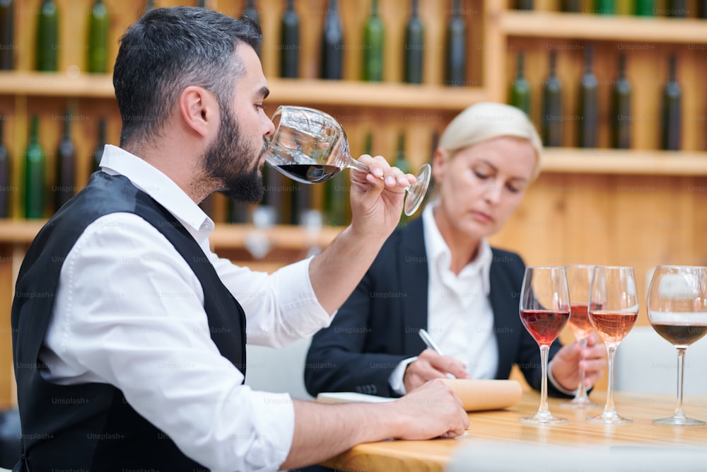 Un jeune sommelier élégant déguste du vin rouge dans l’un des verres pour vérifier sa qualité et sa saveur