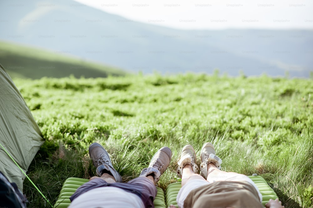 Couple lying on the green meadow while traveling high in the mountains, close-up of a legs in trekking shoes