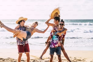 Group of people friends have fun and playing carrying the girls and laughing a lot in friendship - happiness on vacation enjoying the sandy tropical resort beach and clear blue sea in background