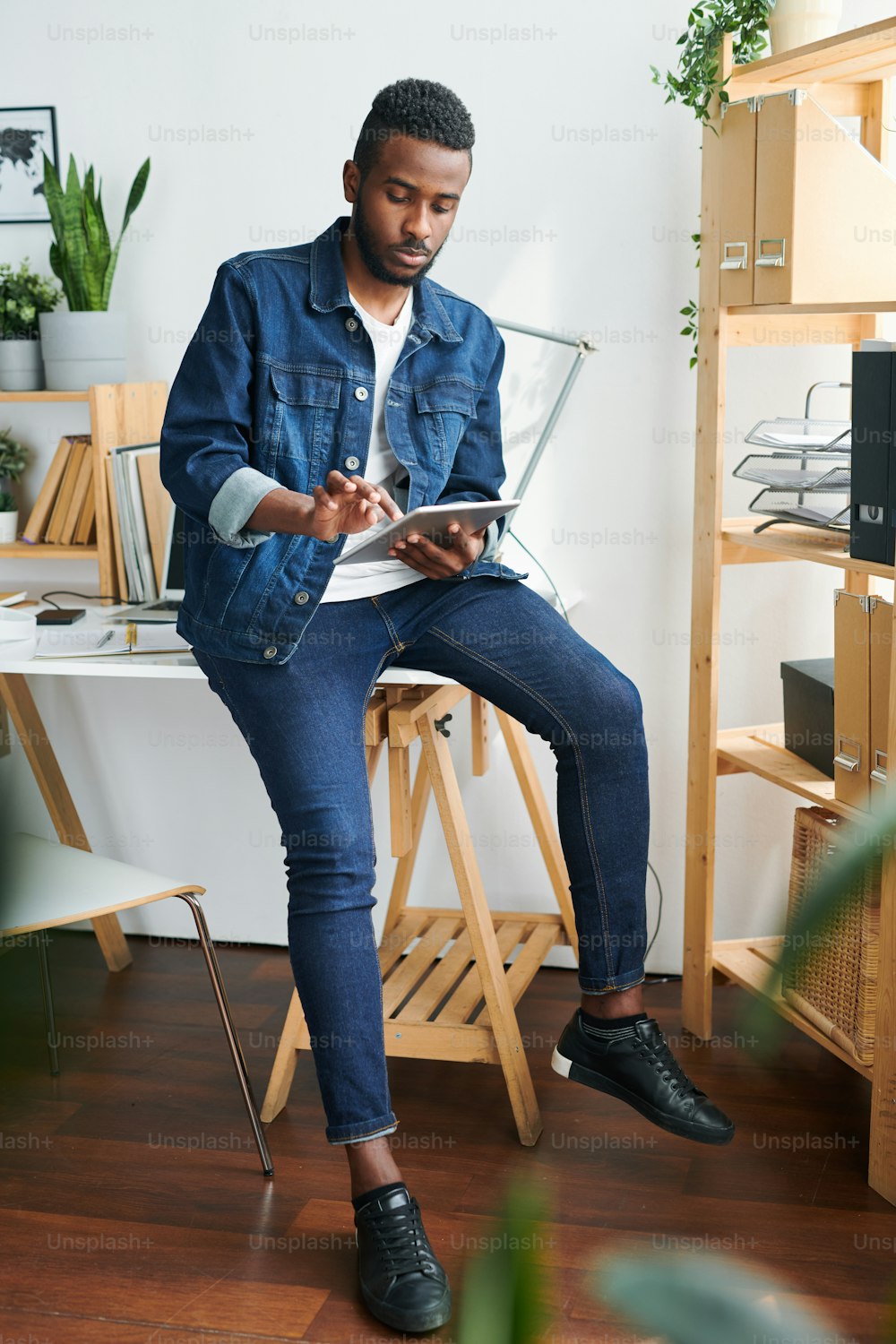 Jovem millennial casual sentado na mesa e pintando no touchpad ou percorrendo sites de design durante o trabalho