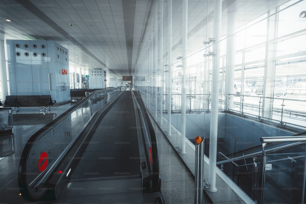 Lange leere Wartehalle in einem Abflugbereich eines modernen Flughafenterminals El Part in Barcelona, Spanien, die zu Flugsteigen mit einem zeitgenössischen Fahrsteig führt, der sich in den Fluchtpunkt erstreckt