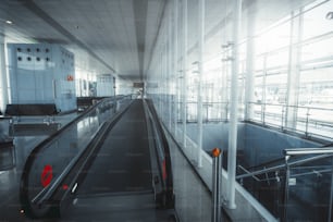 Long empty waiting hall in a departure area of a modern airport terminal El Part in Barcelona, Spain, leading to boarding gates with a contemporary moving travelator stretching into the vanishing point