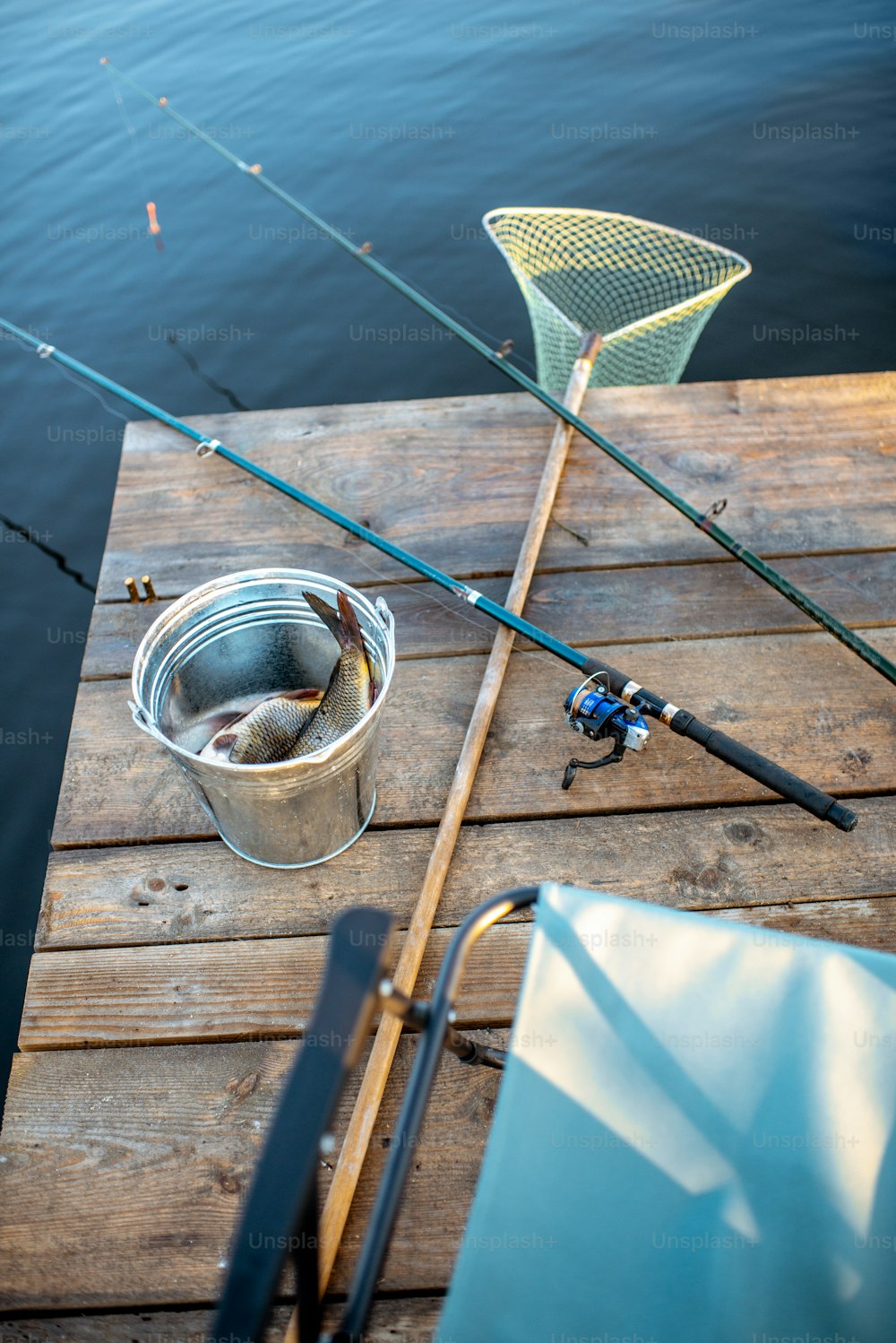 Lugar para pescar con cañas de pescar, red y cubo en el muelle de madera en el lago