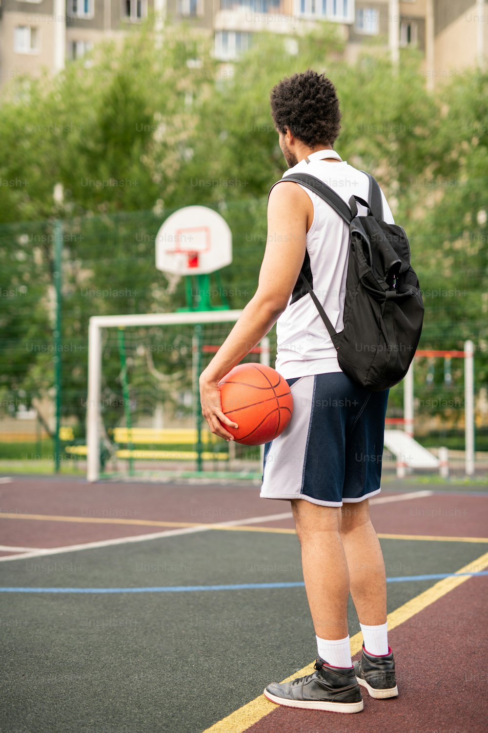 공과 배낭을 멘 젊은 활동적인 남자 농구 선수가 놀이터에 하얀 선 옆에 서 있다
