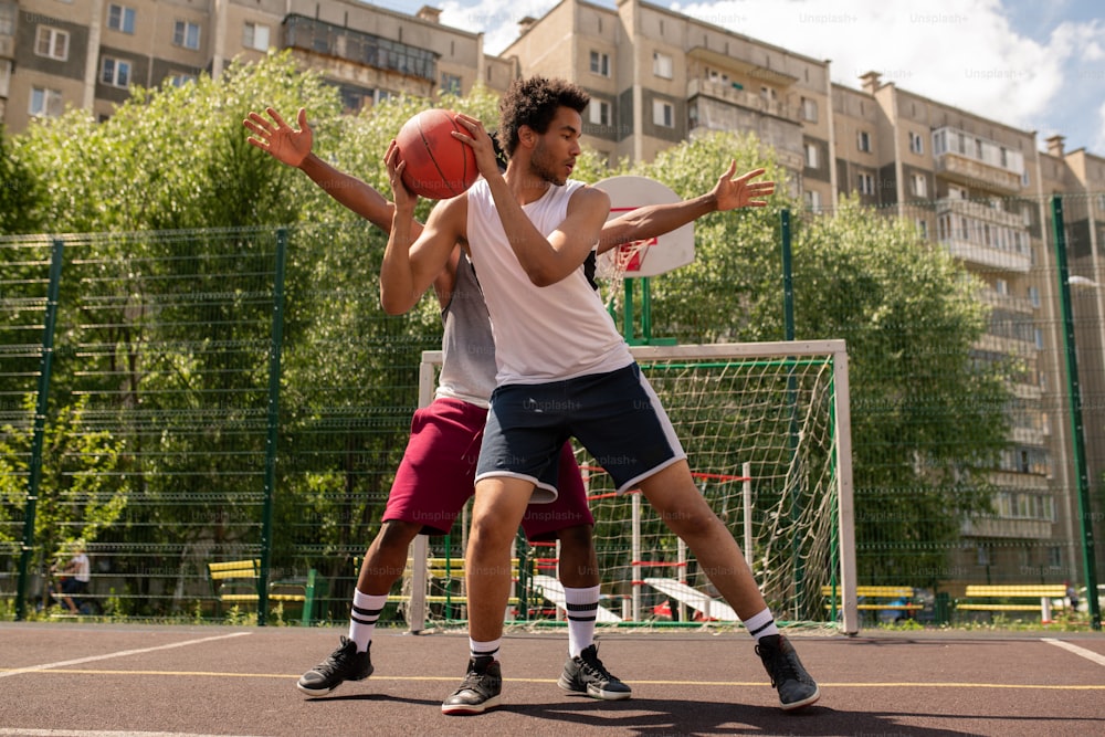 One of basketball players with ball trying not to let his rival take it away during outdoor game