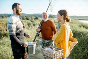 Giovane uomo e donna con il nonno anziano vestito in maglioni che trascorrono un buon tempo insieme mentre pescano al mattino