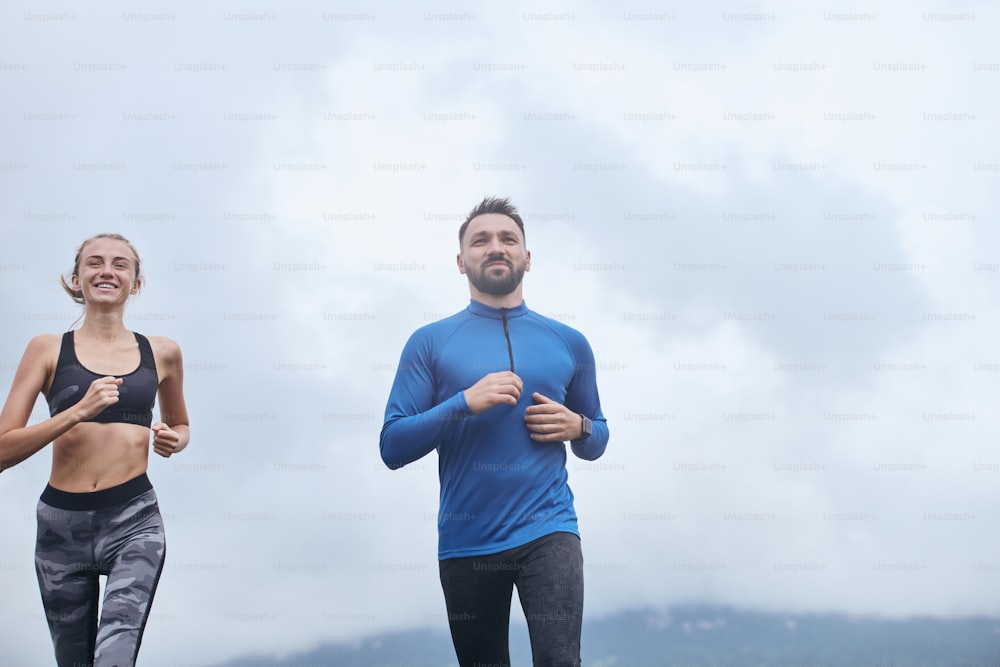 Portrait of two mid age man and woman jogging outdoor, warming up muscules, in summer, on gloomy day, at the road with perspective and scenic view,
