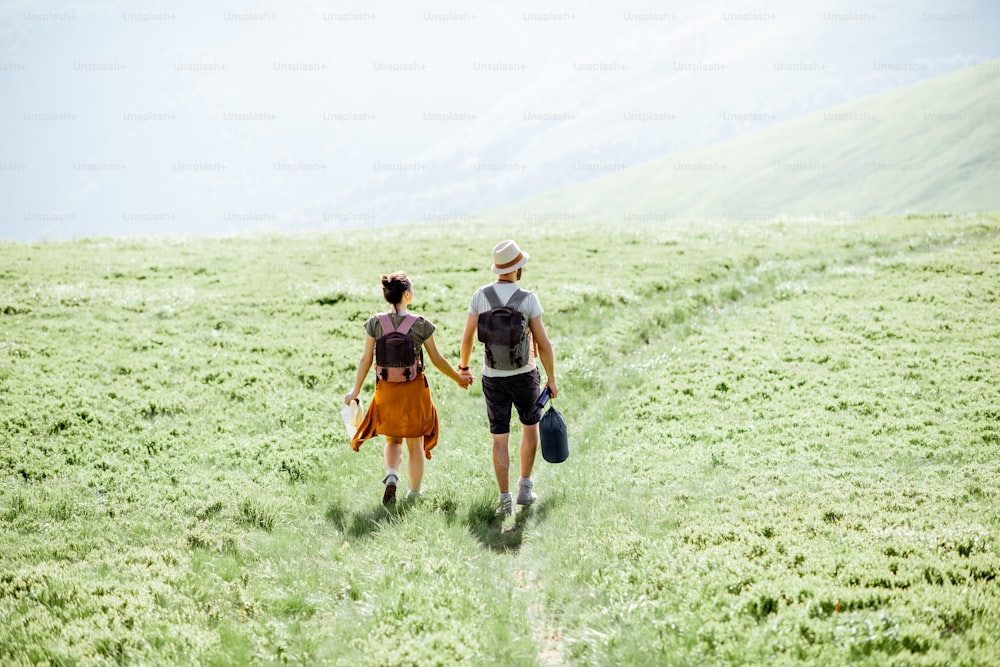Coppia che cammina con zaini sul prato verde, in viaggio in montagna durante il periodo estivo, ampia vista del paesaggio