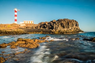 海岸に古典的な灯台と青いオセンと空を背景に美しい風光明媚な風景 – 観光のための旅行と休暇のコンセプト – 波と岩