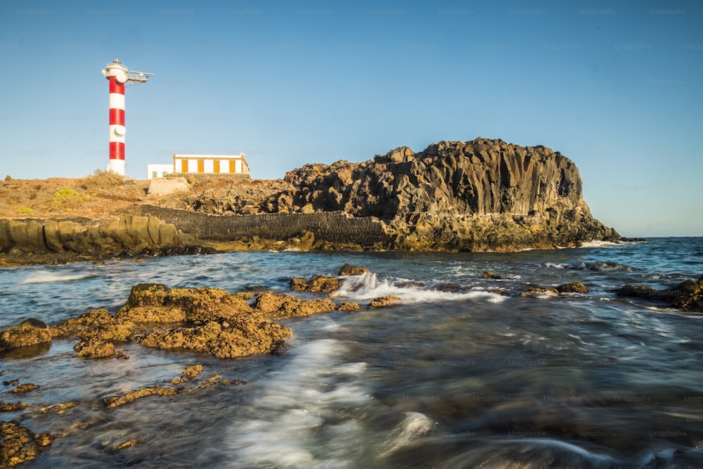 Beautiful scenic landscape with classic lighthouse on the coast and blue ocen and sky in background - concept of travel and vacation for tourism - wave and rocks