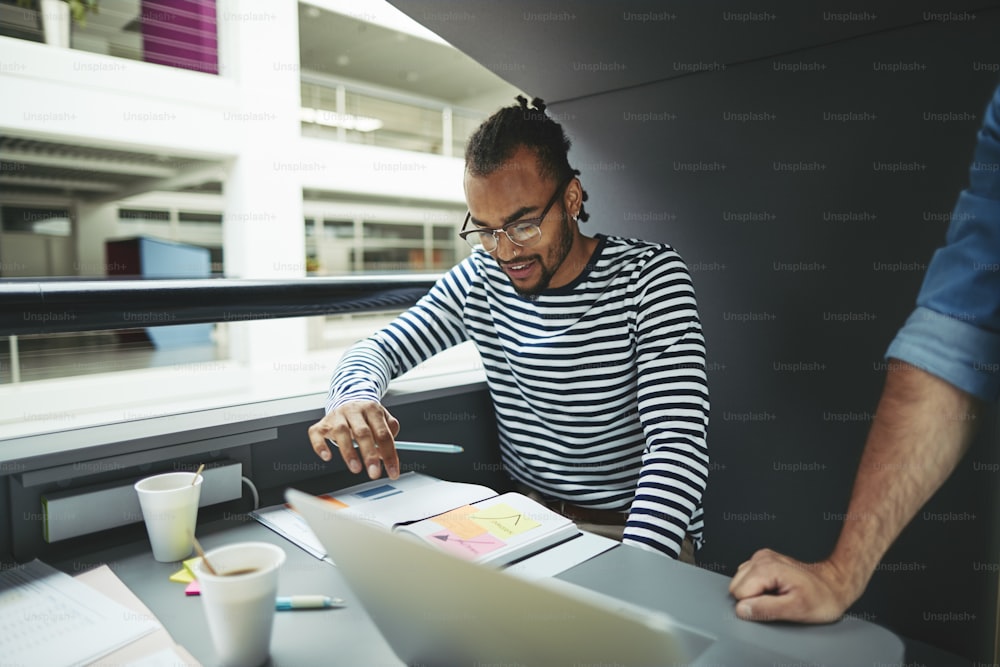 Focused young African American businessman going over notes while working with colleagues in an office pod