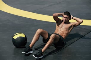 Sport man doing abs crunches exercise, fitness workout at street. Male athlete exercising on yoga mat, doing abdomen muscle training outdoors at gym