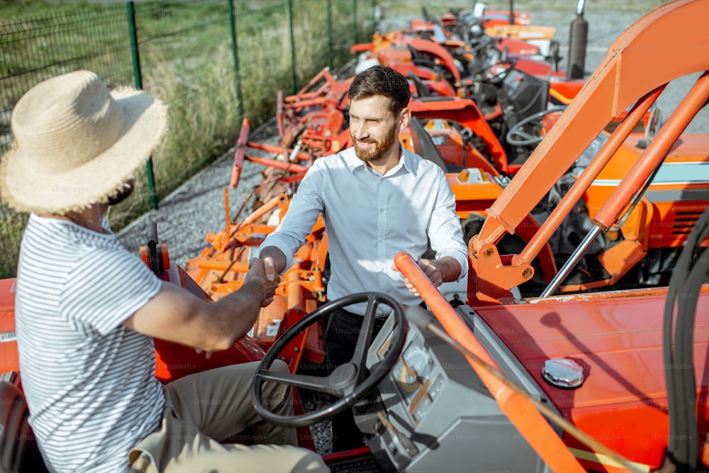 Junger Agronom mit elegantem Verkäufer, der einen Traktor für die Landwirtschaft auf dem offenen Gelände eines landwirtschaftlichen Geschäfts wählt