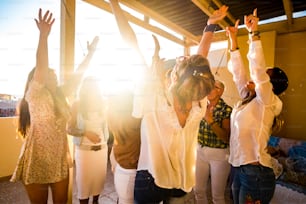 Active happy group of young free caucasian people woman celebrate and dance all together with friendship - sunset in backlight for party at home concept - Happiness for group