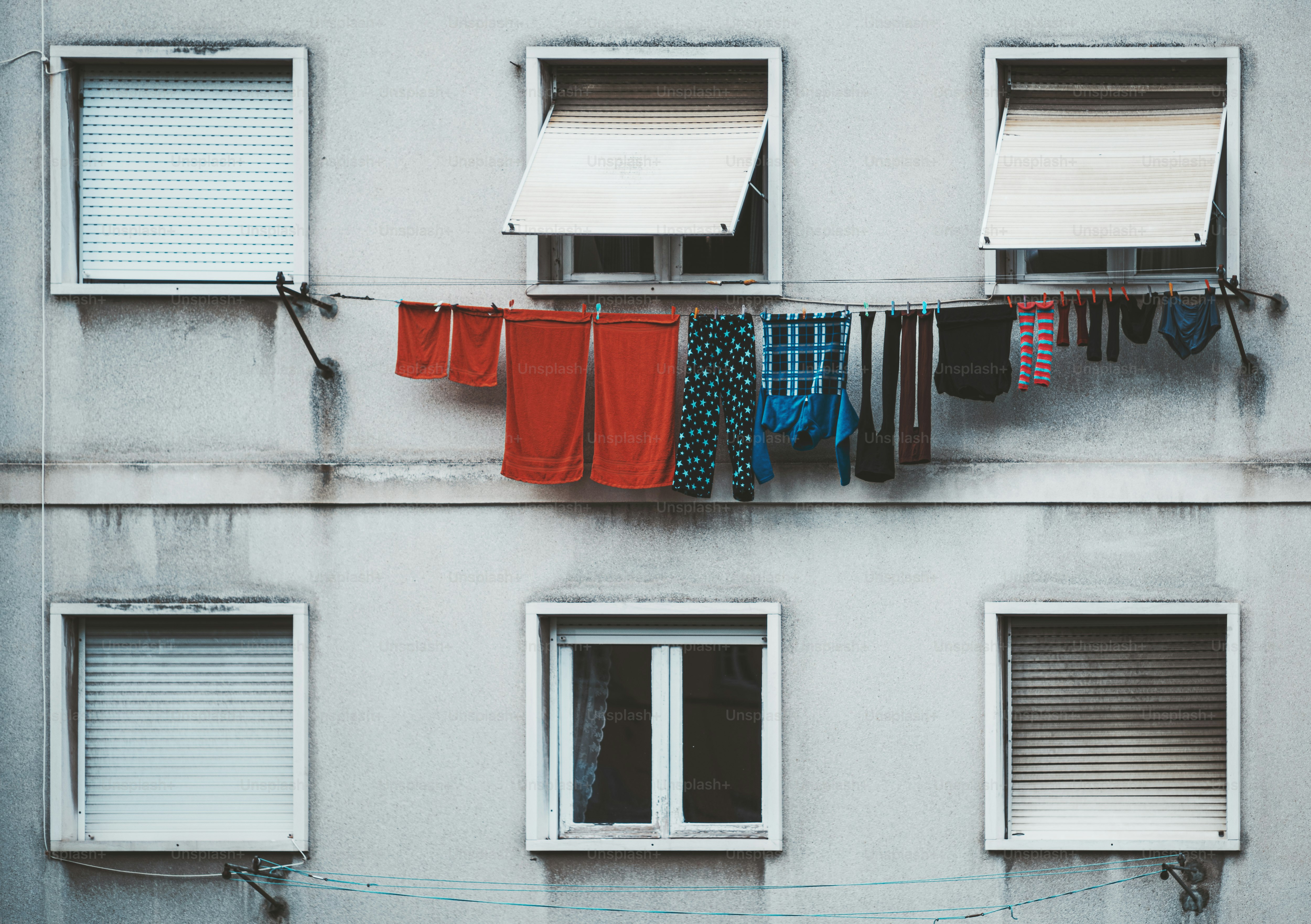 Nahaufnahme einer Fassade eines gewöhnlichen Wohnhauses in Lissabon mit zwei Fensterreihen und der Reihe mit trocknenden bunten Kleidern an einem Sommertag, Portugal