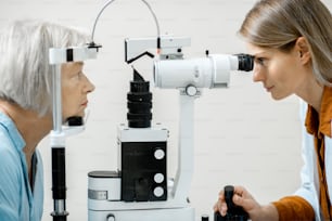 안과 사무실에서 건강 검진 중 현미경을 사용하여 노인 환자의 눈을 검사하는 안과 의사