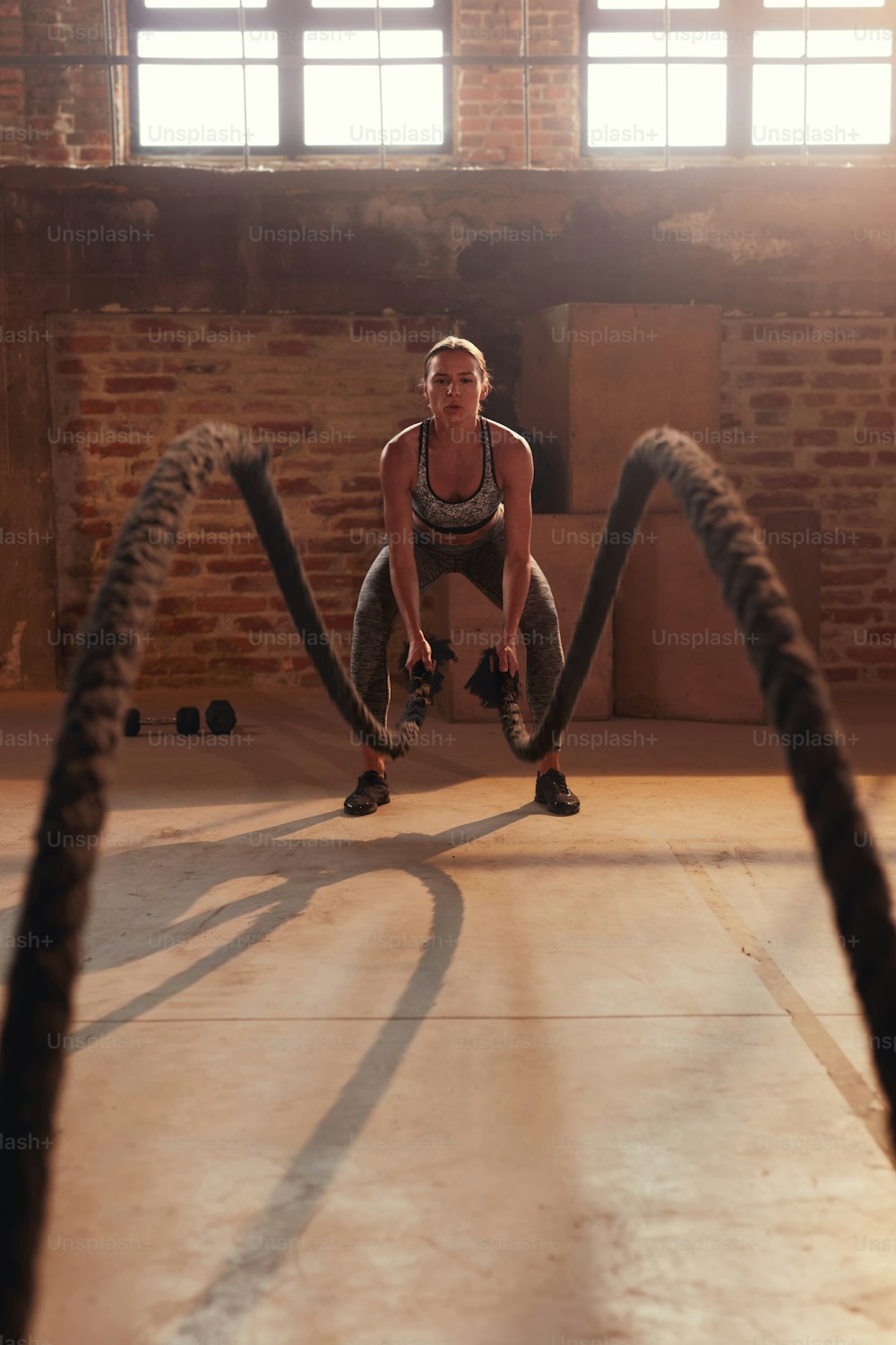Fitness workout. Sport woman doing battle rope exercise at gym. Girl athlete with fit body exercising, doing functional training with heavy ropes indoors