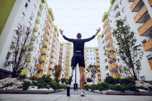 Vista trasera del apuesto deportista con pierna artificial de pie con las manos en el aire libre rodeado de edificios.