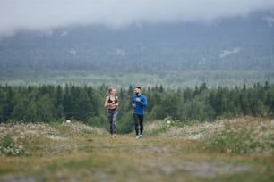 Two mid age man and woman jogging outdoor, warming up muscules, in summer, on gloomy day, at the road with perspective and scenic view, full length