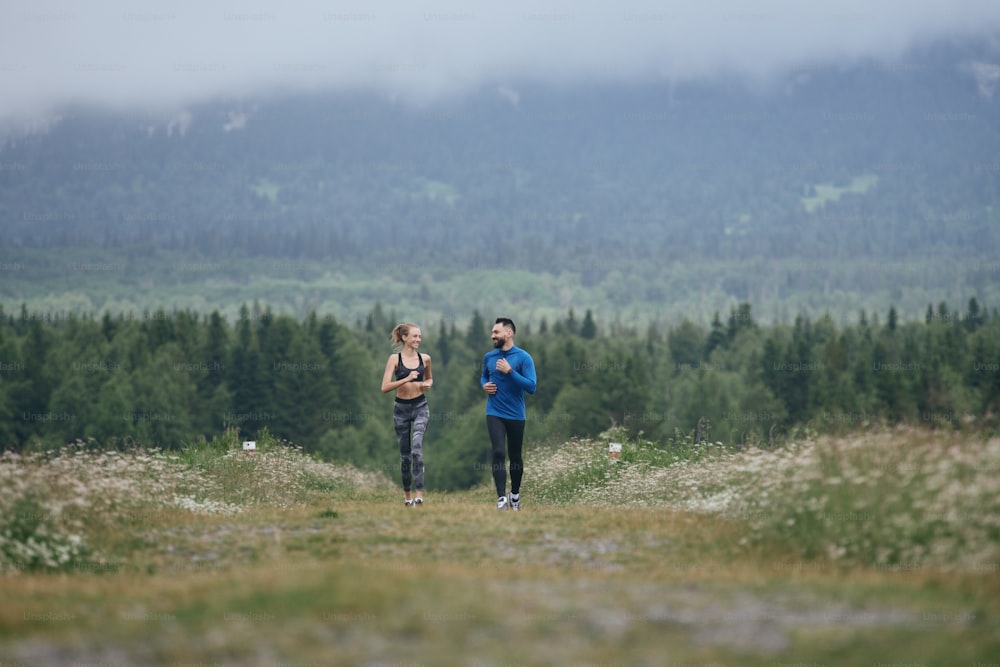 Due uomini e donne di mezza età che fanno jogging all'aperto, riscaldando i muscoli, in estate, in una giornata uggiosa, sulla strada con prospettiva e vista panoramica, a tutta lunghezza