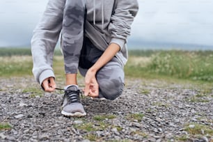 Mid age woman tying shoelaces , getting ready for work out outdoor, she is at the country road with scenic view