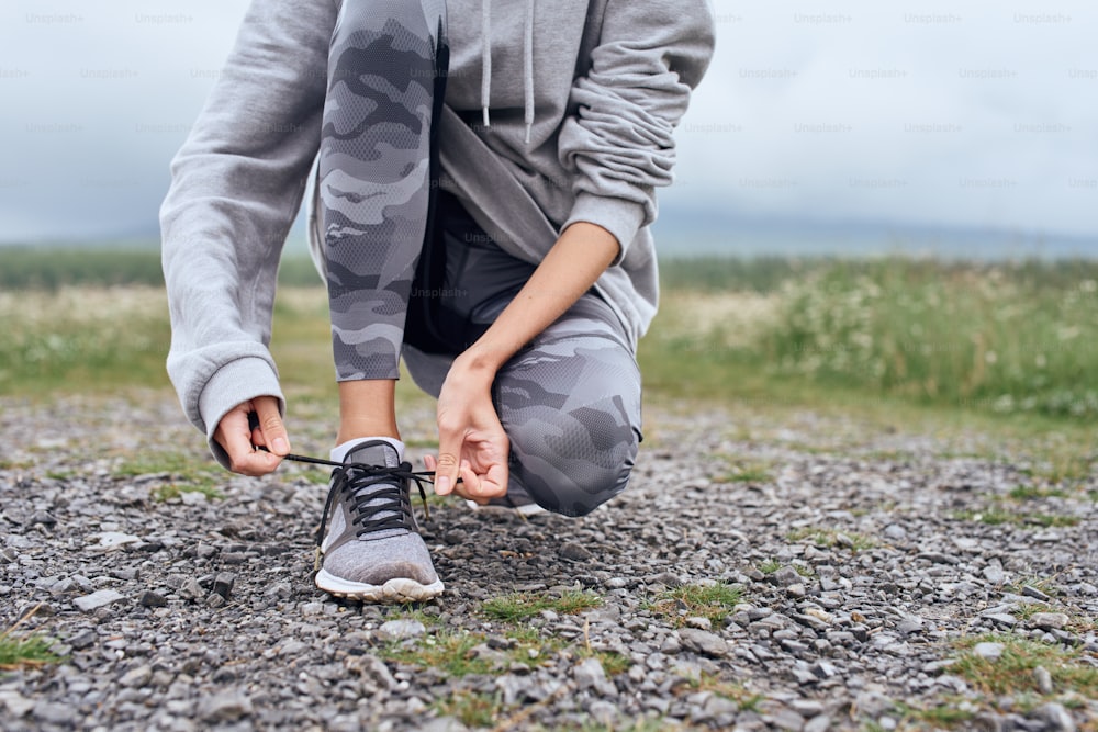 Mid age woman tying shoelaces , getting ready for work out outdoor, she is at the country road with scenic view