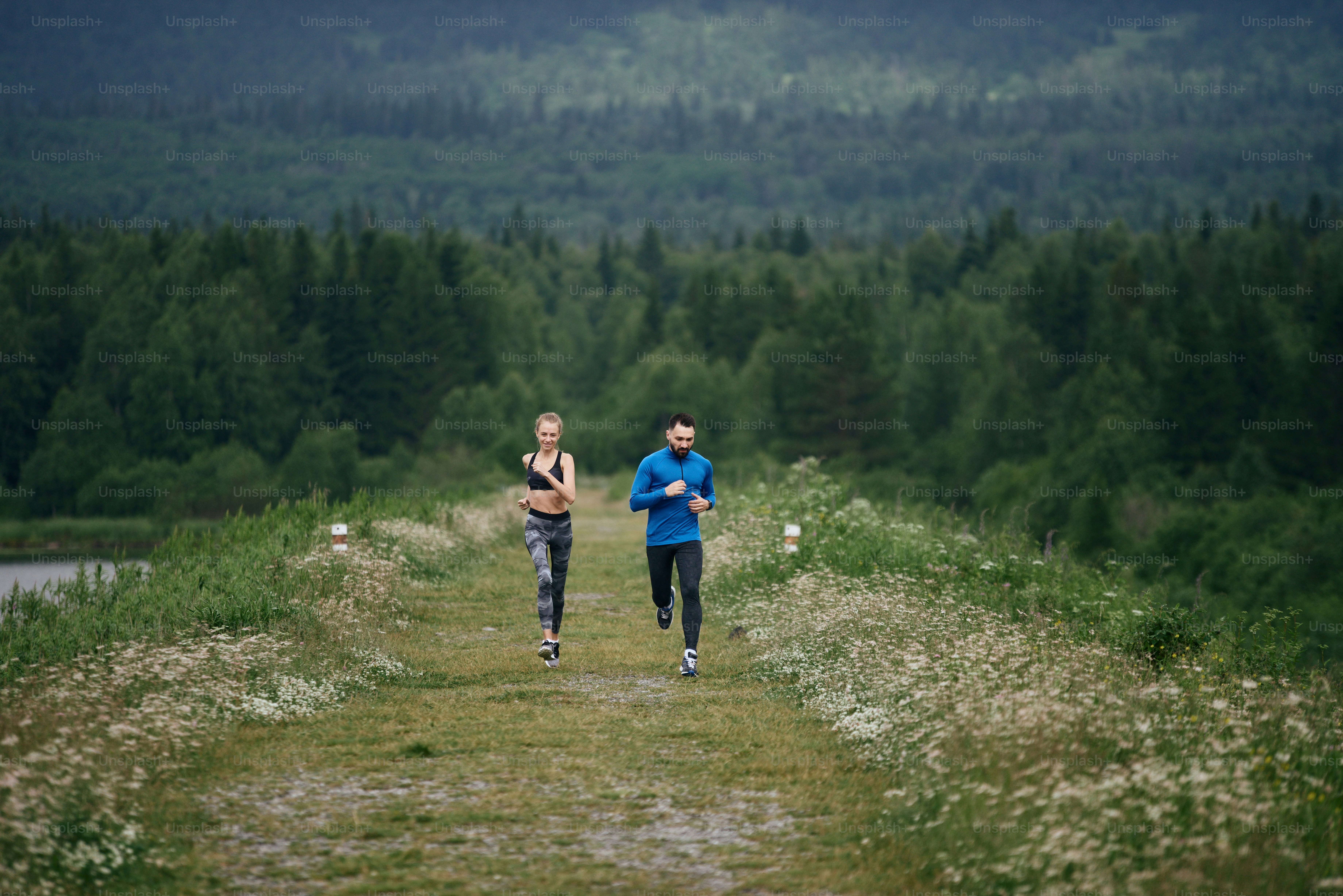 Two mid age man and woman jogging outdoor, warming up muscules, in summer, on gloomy day, at the road with perspective and scenic view, full length